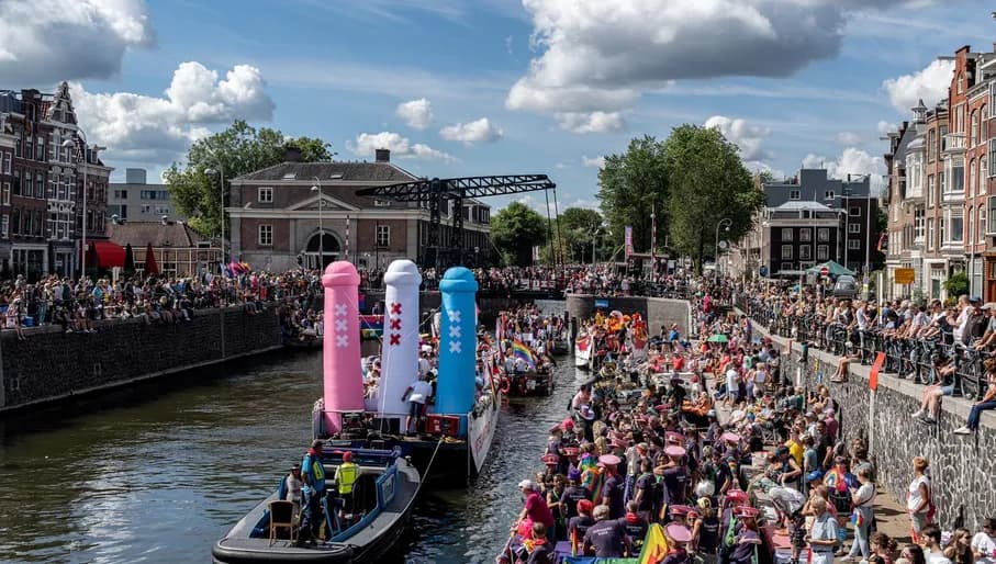 A crowd of people on the streets and in a boat with flags and signs - Pride Canal Parade