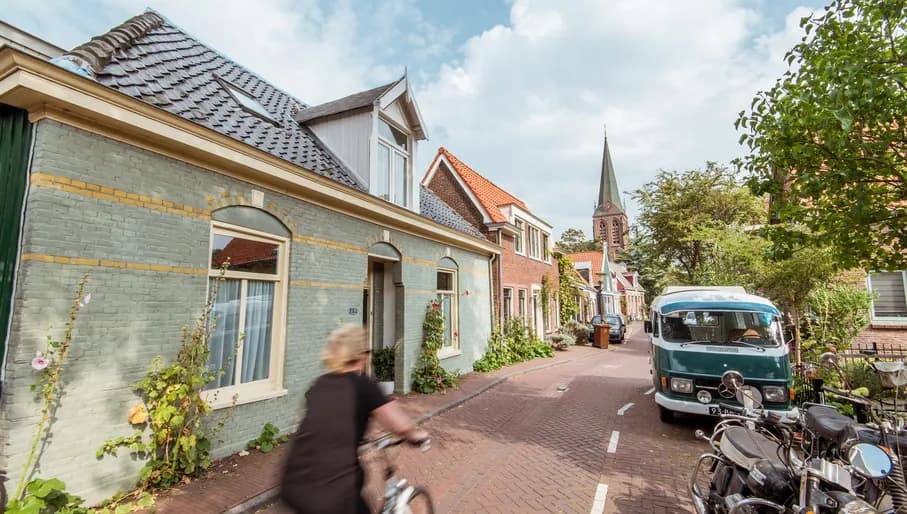 Woman cycling on Nieuwendammerdijk past Blue House traditional houses